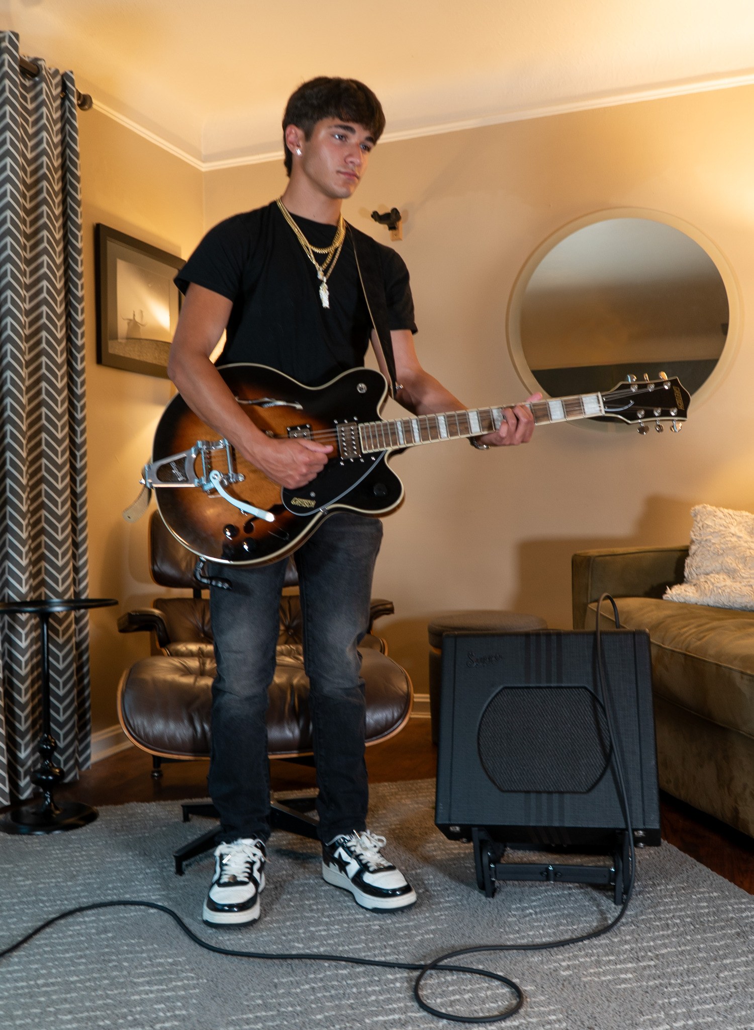 Musician playing guitar beside an amplifier supported by AmpTiltor™